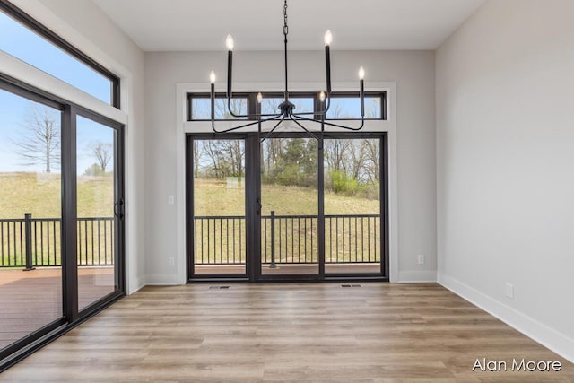 unfurnished dining area with an inviting chandelier, baseboards, wood finished floors, and visible vents