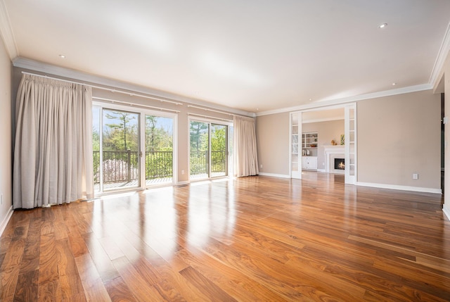 unfurnished living room with crown molding, baseboards, and a lit fireplace