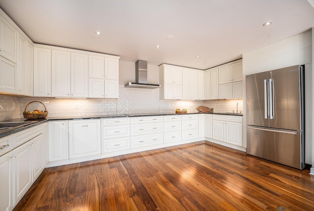kitchen featuring freestanding refrigerator, dark countertops, dark wood-type flooring, wall chimney exhaust hood, and a sink