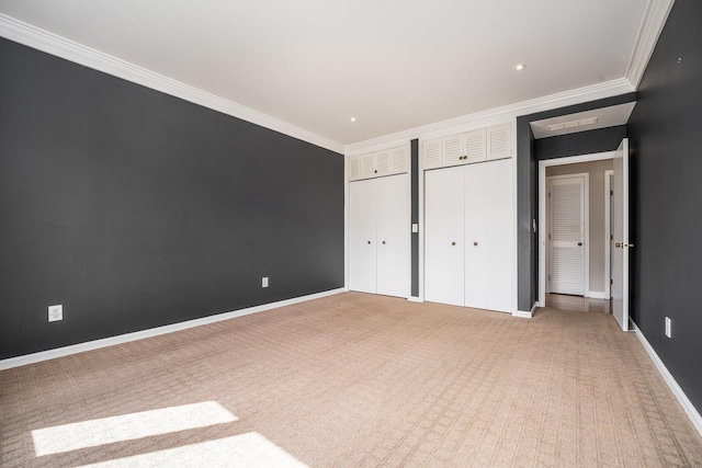 unfurnished bedroom featuring crown molding, baseboards, multiple closets, and light carpet