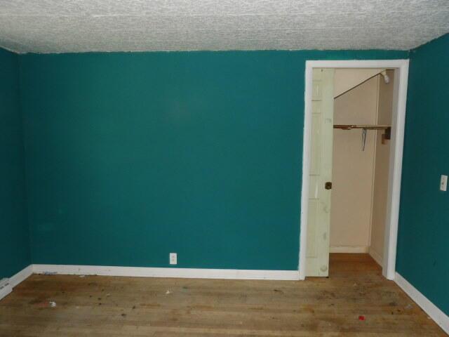 unfurnished bedroom featuring baseboards, a textured ceiling, wood finished floors, and a closet