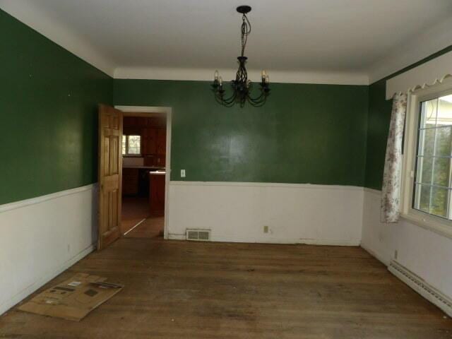 empty room featuring visible vents, wainscoting, wood finished floors, a baseboard radiator, and a notable chandelier