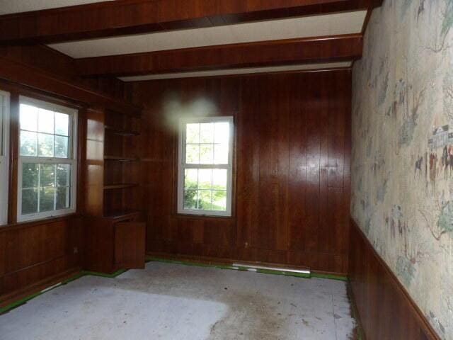 empty room featuring wooden walls, beamed ceiling, and wallpapered walls