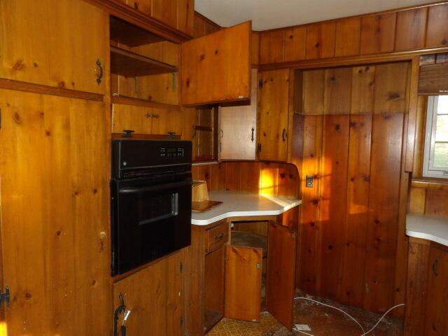 kitchen featuring brown cabinets, black oven, wooden walls, and light countertops