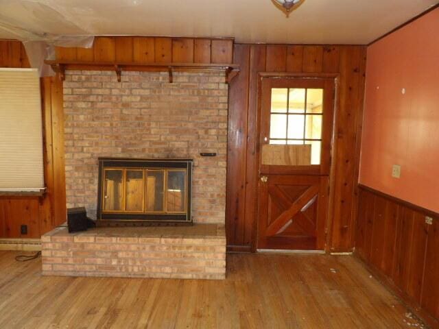 unfurnished living room featuring a brick fireplace, wood walls, and wood finished floors
