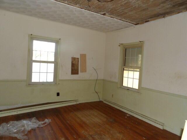 spare room featuring a healthy amount of sunlight, baseboard heating, and wood finished floors