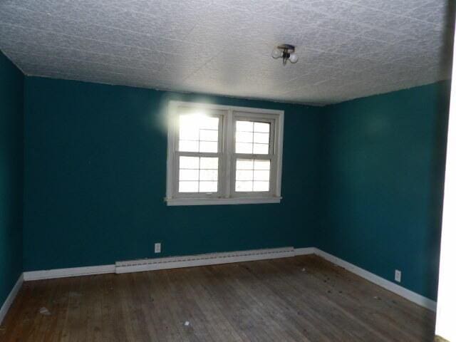 spare room featuring baseboard heating, baseboards, wood finished floors, and a textured ceiling