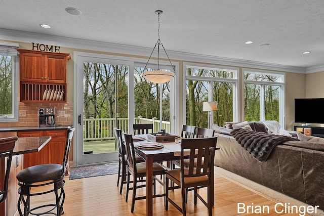 dining space featuring light wood-type flooring, ornamental molding, and a healthy amount of sunlight