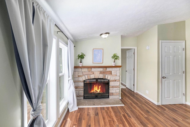 living room featuring lofted ceiling, wood finished floors, a fireplace, baseboards, and a textured ceiling