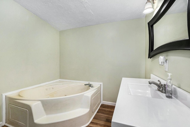 bathroom featuring vanity, a textured ceiling, baseboards, wood finished floors, and a garden tub