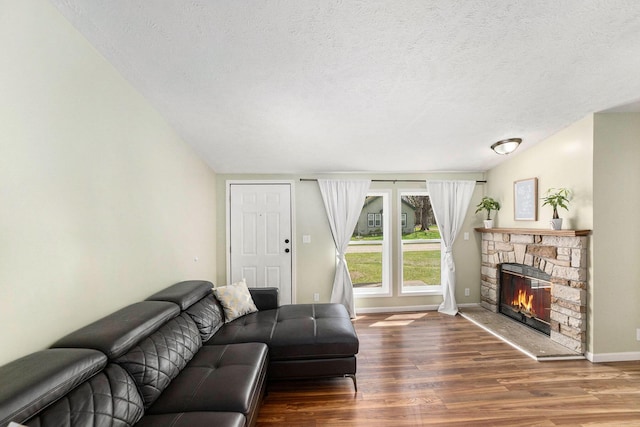 living area with a textured ceiling, baseboards, a stone fireplace, and wood finished floors