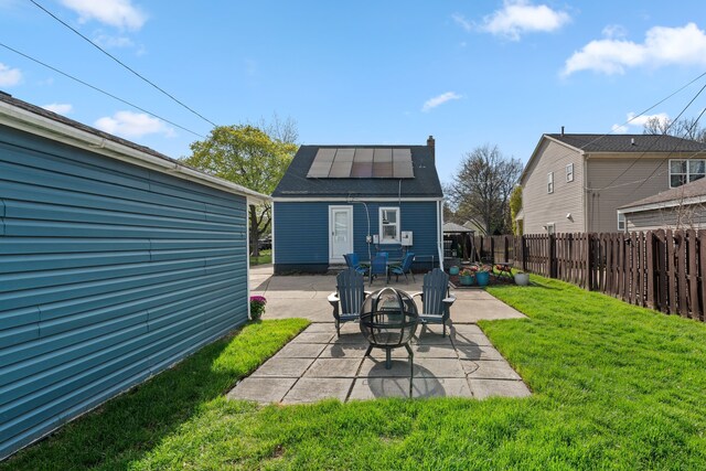 rear view of house featuring fence private yard, solar panels, a lawn, a patio, and a fire pit