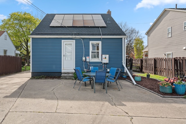 rear view of property with fence, a shingled roof, solar panels, and a patio area