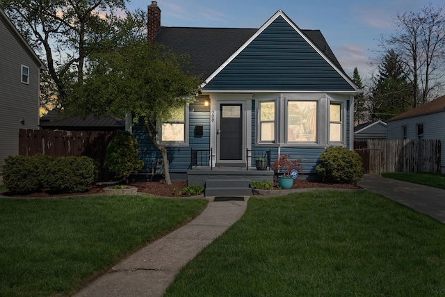 bungalow-style house featuring roof with shingles, fence, a chimney, and a front yard