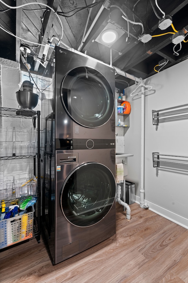 laundry area with baseboards, stacked washer / drying machine, wood finished floors, and laundry area