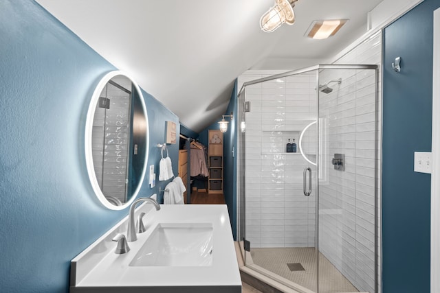 full bath with a sink, a walk in closet, vaulted ceiling, and a shower stall