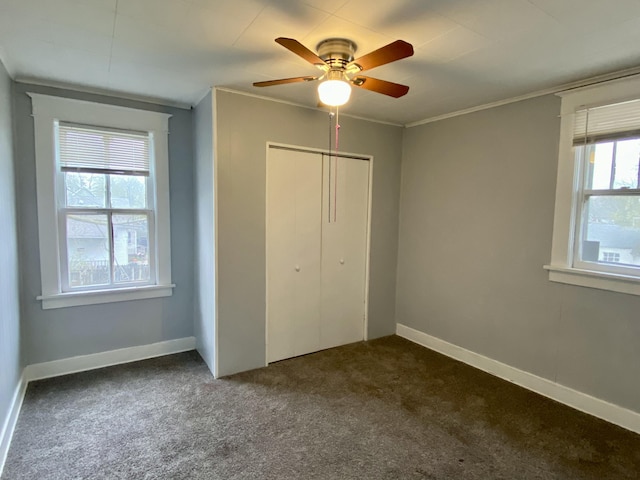 unfurnished bedroom featuring a ceiling fan, ornamental molding, dark carpet, and a closet