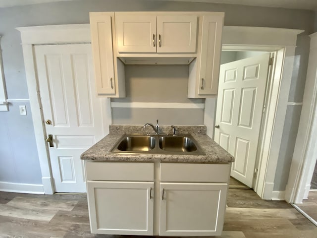 kitchen featuring a sink, baseboards, white cabinets, and wood finished floors