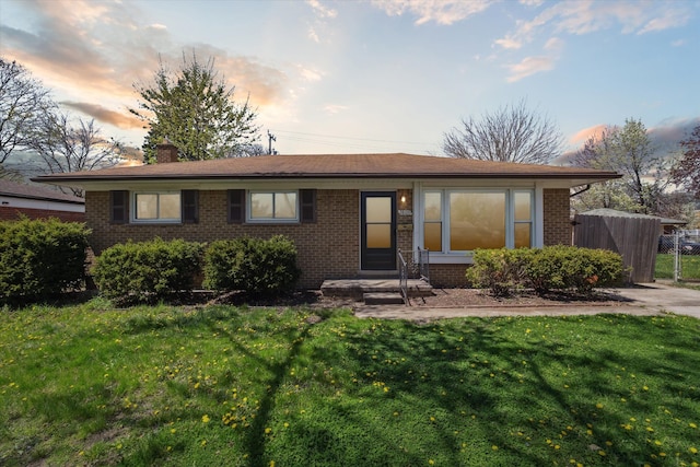 single story home featuring brick siding, a lawn, fence, and a chimney