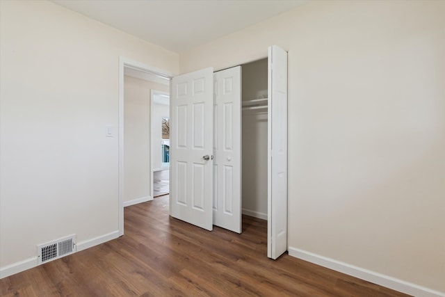 unfurnished bedroom with baseboards, a closet, wood finished floors, and visible vents