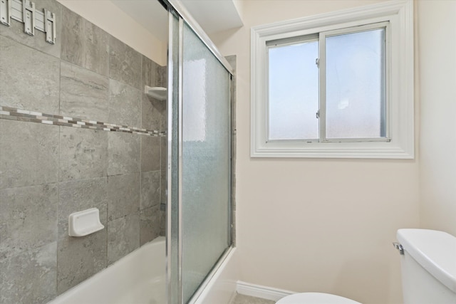 bathroom featuring bath / shower combo with glass door, baseboards, and toilet