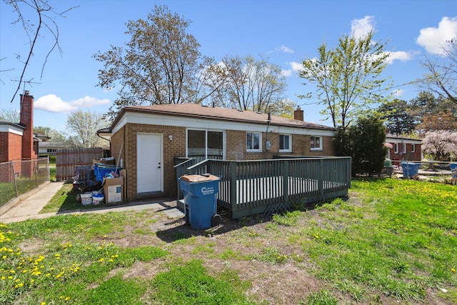 rear view of property with fence, a wooden deck, a yard, and brick siding