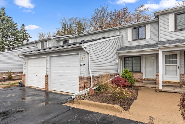 view of property with brick siding, a garage, and aphalt driveway