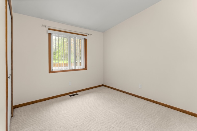 carpeted empty room with visible vents, baseboards, and vaulted ceiling