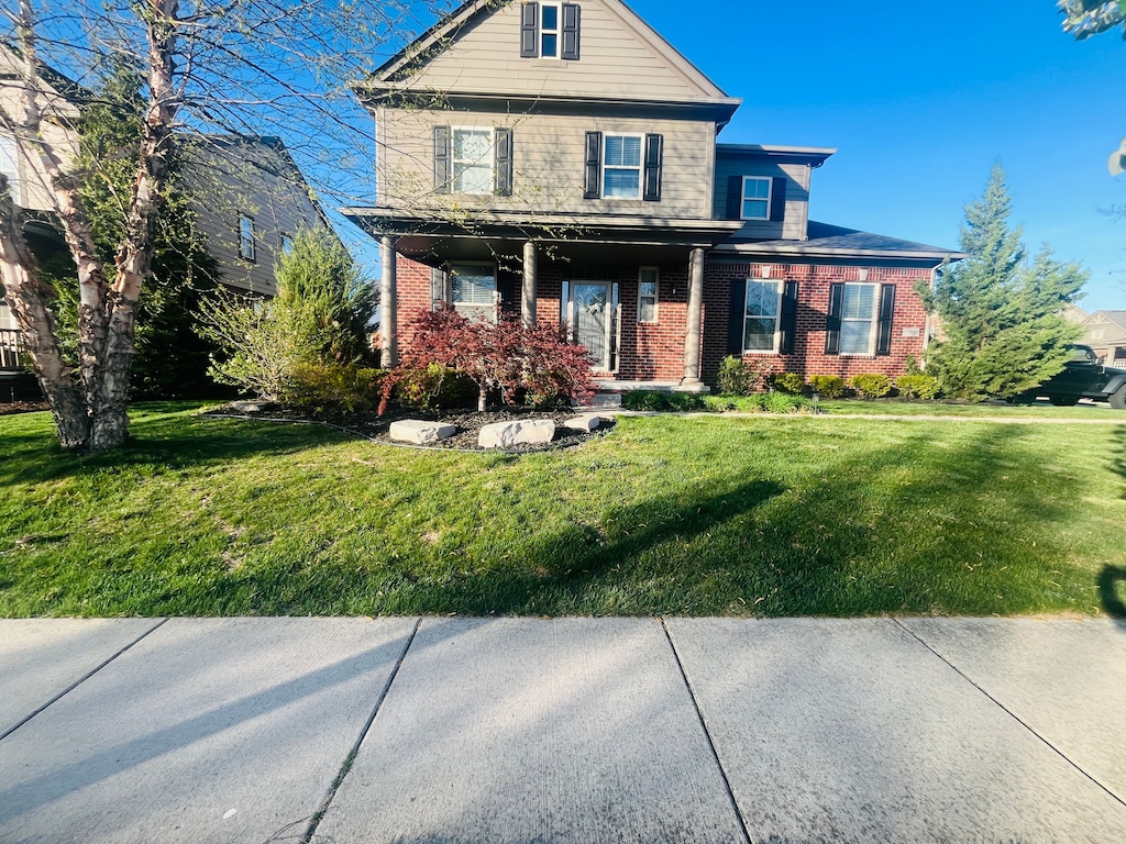 view of front of property with a front yard, a porch, and brick siding