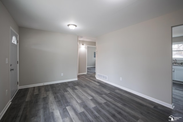 empty room with a sink, baseboards, dark wood finished floors, and visible vents