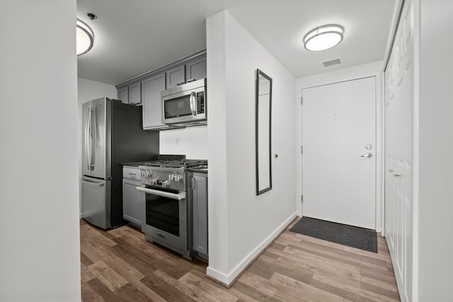 kitchen with stainless steel appliances, wood finished floors, dark countertops, gray cabinets, and baseboards
