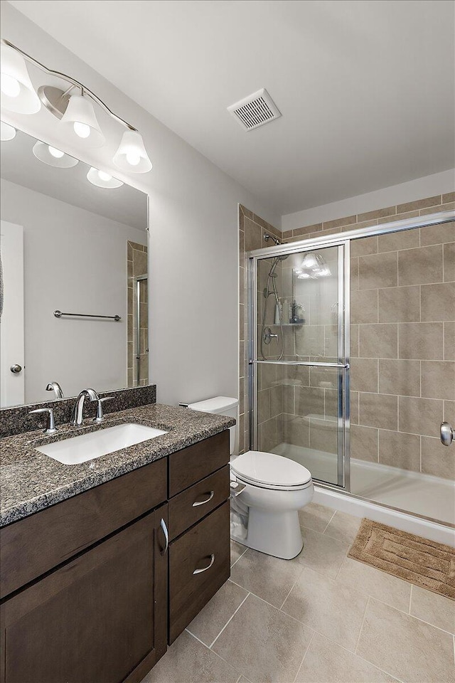 bathroom featuring tile patterned flooring, vanity, toilet, a shower stall, and visible vents