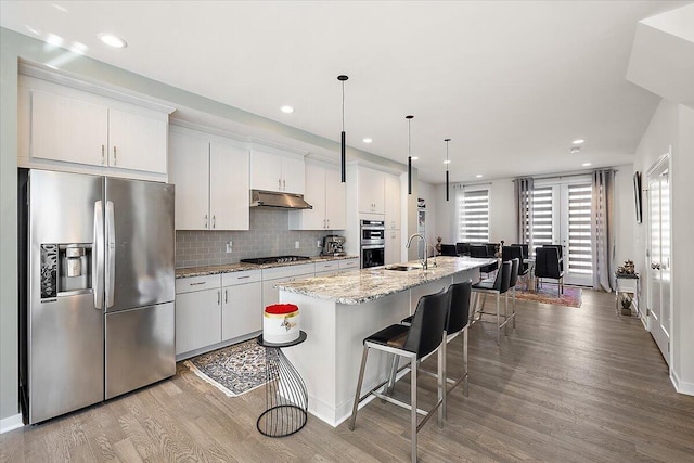 kitchen featuring a kitchen island with sink, a kitchen breakfast bar, under cabinet range hood, a sink, and stainless steel appliances