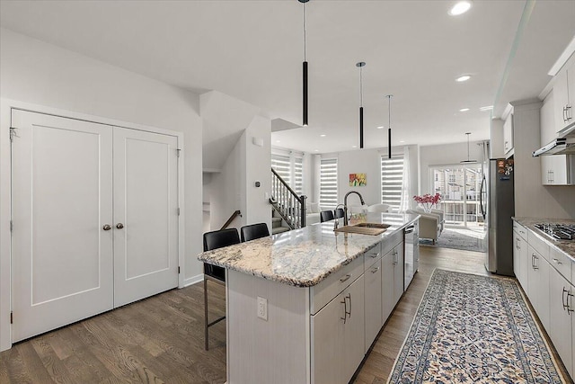 kitchen featuring a kitchen island with sink, a kitchen bar, dark wood-type flooring, a sink, and stainless steel appliances
