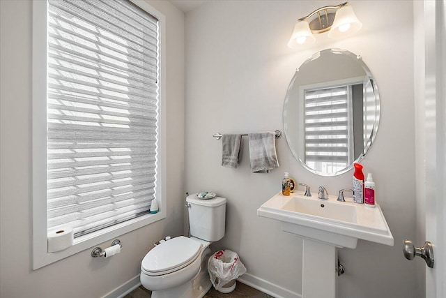 bathroom featuring toilet, baseboards, and a healthy amount of sunlight