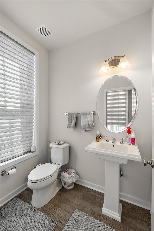 half bathroom featuring baseboards, toilet, wood finished floors, and visible vents