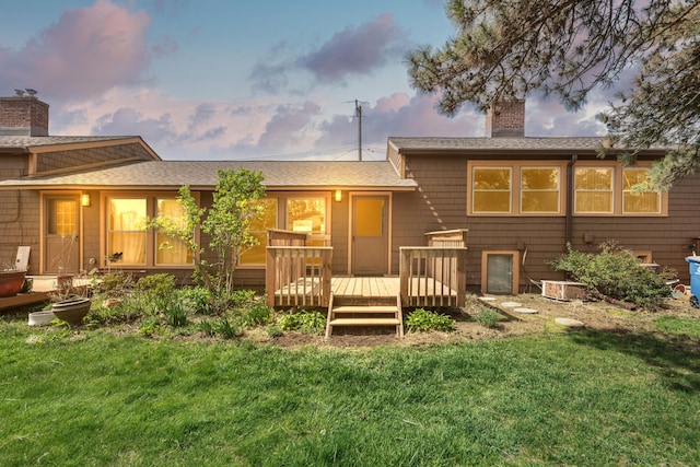 back of house at dusk featuring a lawn, roof with shingles, a wooden deck, and a chimney