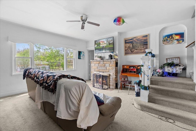 carpeted living room with ceiling fan, stairs, and a stone fireplace