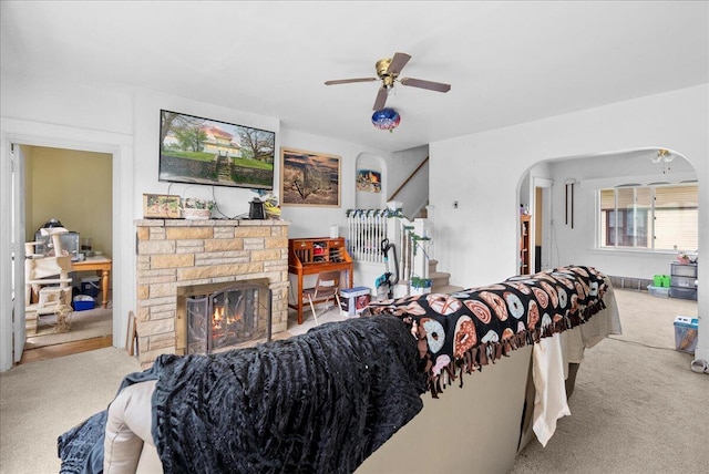 carpeted living room featuring a ceiling fan, arched walkways, and a fireplace