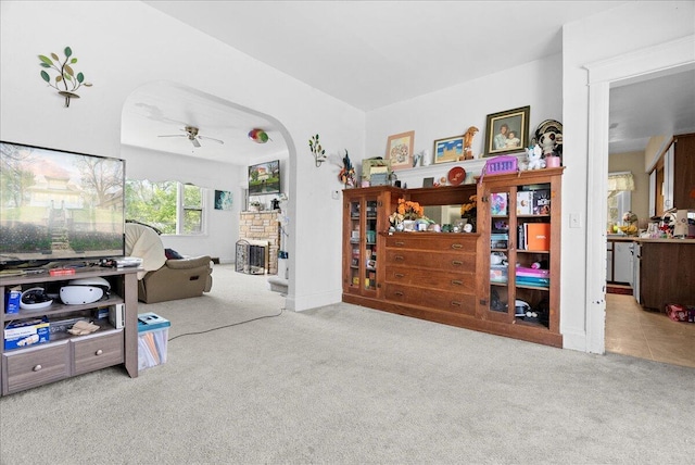 living area with arched walkways, ceiling fan, carpet, and a fireplace