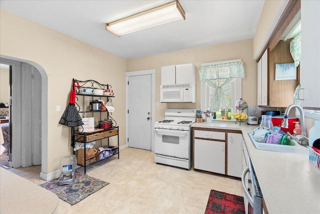 kitchen with white appliances, light countertops, arched walkways, white cabinets, and a sink
