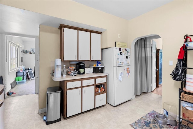 kitchen featuring freestanding refrigerator, white cabinetry, arched walkways, and light countertops
