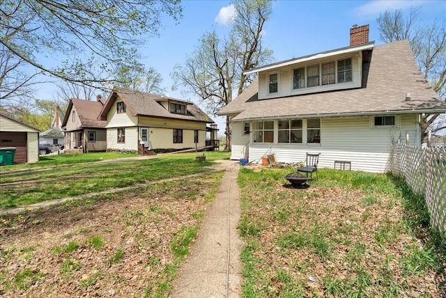 back of property featuring fence, a chimney, a yard, and an outdoor fire pit