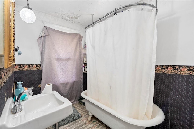 bathroom with wallpapered walls, a sink, curtained shower, and a soaking tub