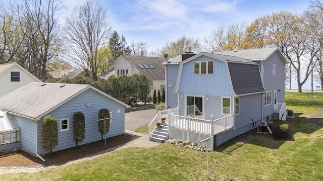 back of house with a lawn, a wooden deck, a shingled roof, and a gambrel roof