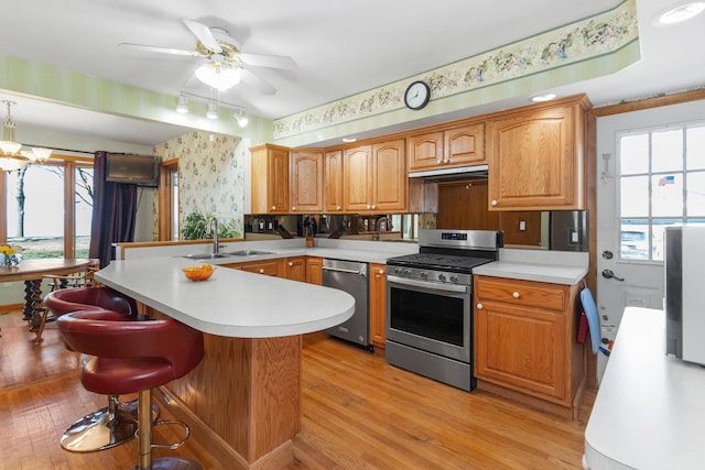 kitchen featuring a sink, light countertops, stainless steel appliances, wallpapered walls, and a peninsula