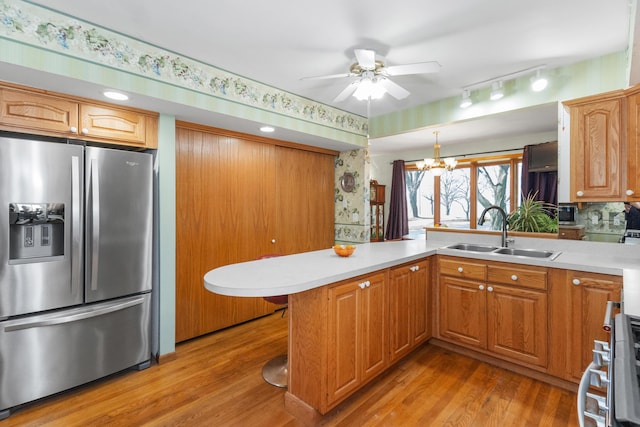 kitchen featuring a peninsula, light countertops, stainless steel fridge with ice dispenser, a sink, and ceiling fan with notable chandelier