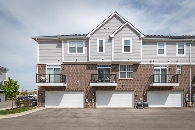 view of front of property with an attached garage, central air condition unit, driveway, and brick siding