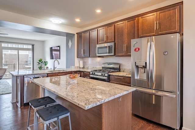 kitchen with a sink, light stone countertops, stainless steel appliances, and a peninsula