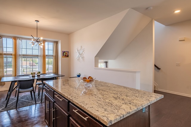 kitchen with light stone counters, a chandelier, a center island, decorative light fixtures, and dark wood-style floors